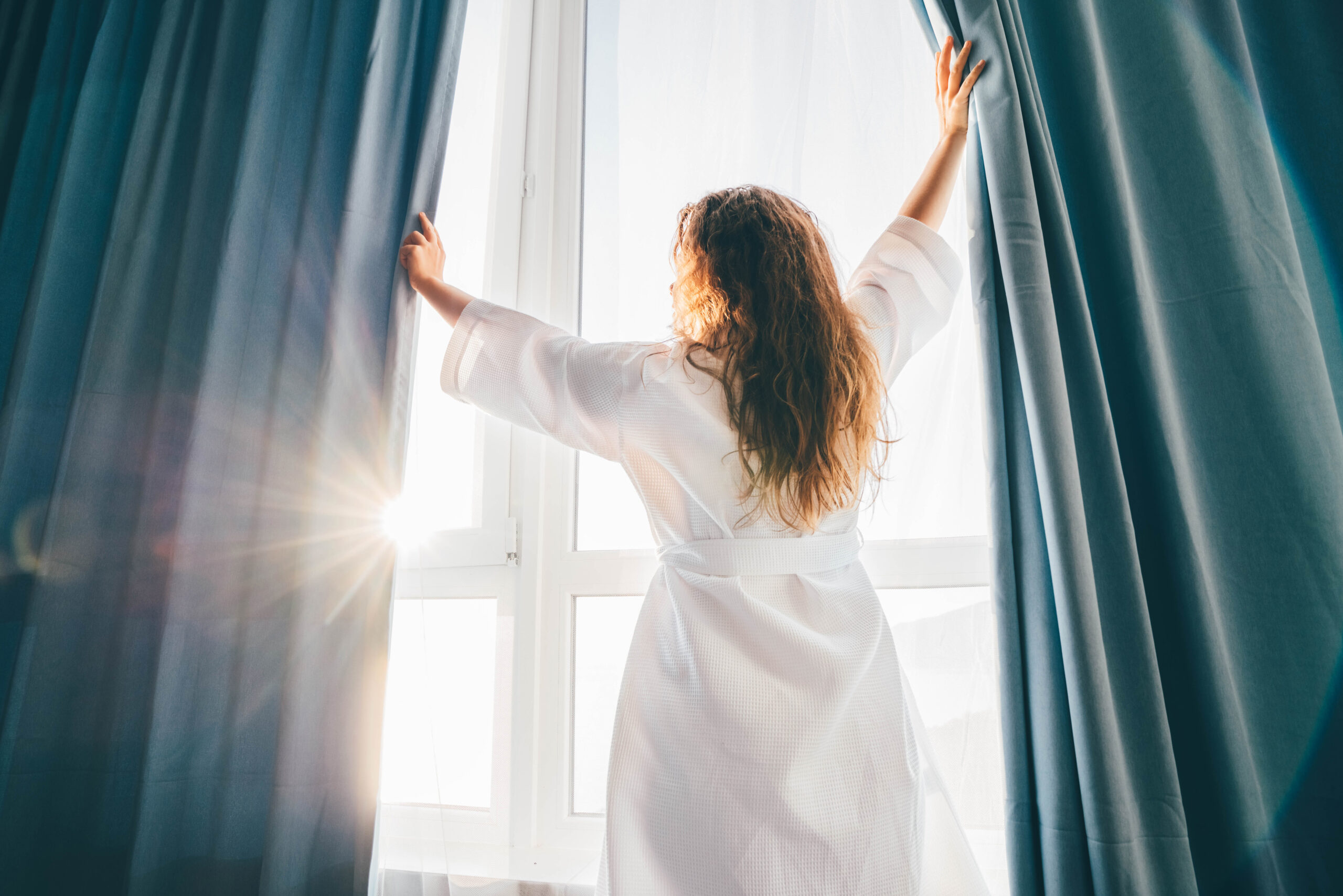 Woman-in-bathrobe-opening-curtains